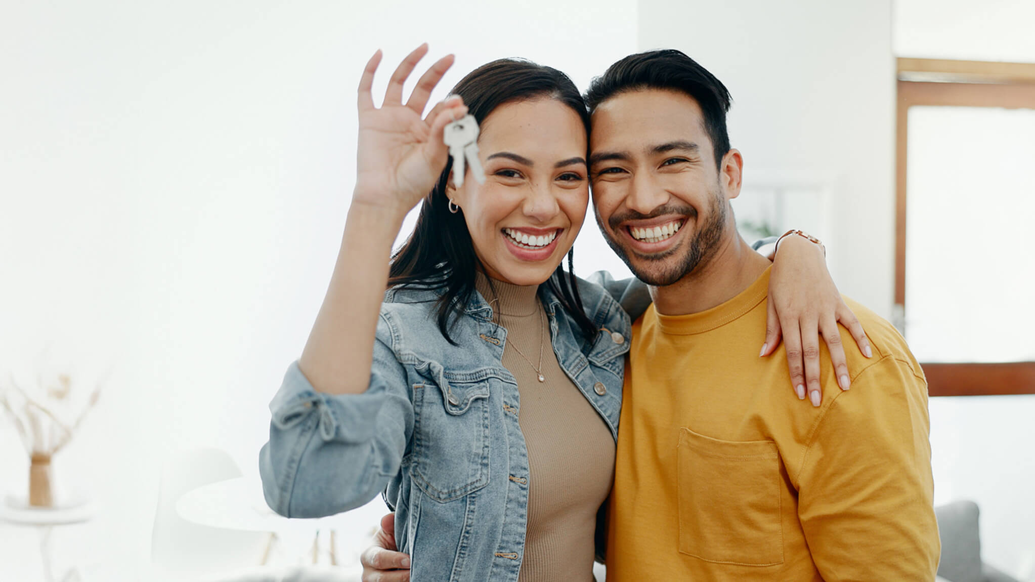 Younger couple with arms around each other holding up keys
